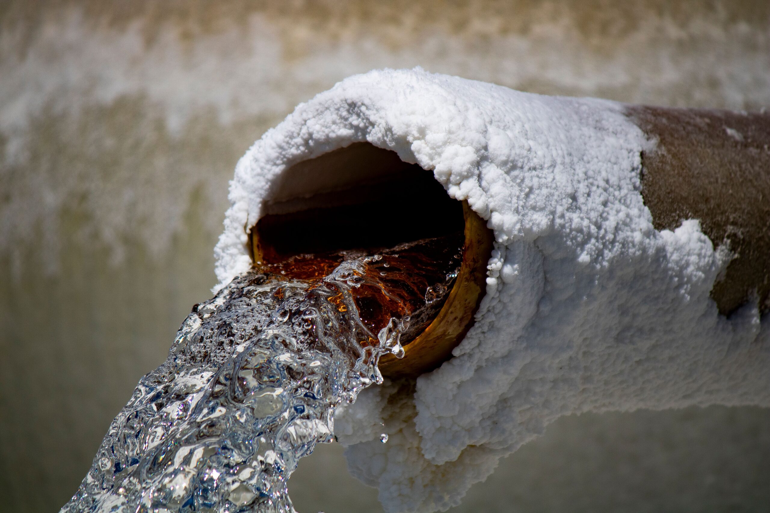 Eau s'écoulant d'une conduite rouillée couverte de dépôts blancs