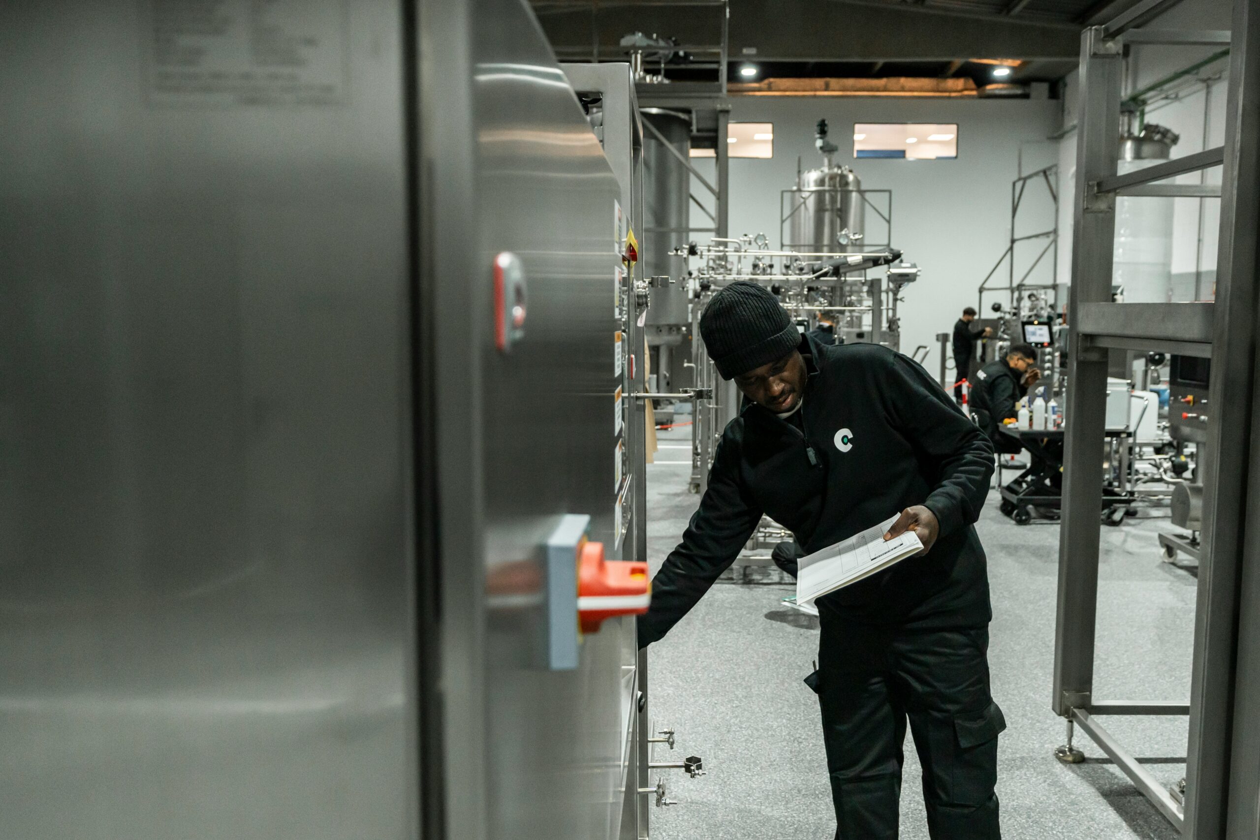tecnic-bioprocess-solutions--Wt8AyCr9i4-unsplash Technicien inspectant une armoire en inox, carnet en main, dans une salle de bioprocédés